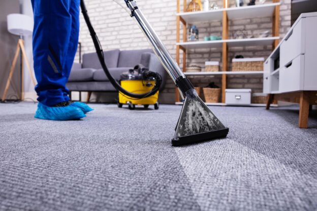 Profissional realizando a lavagem profissional de carpetes com equipamento a vapor em ambiente residencial.