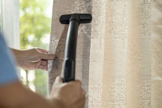 Limpeza de cortina sendo realizada com aspirador para remoção de poeira acumulada