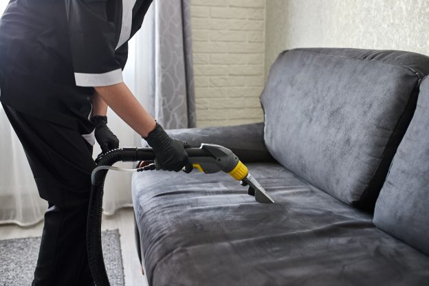 Profissional realizando lavagem de sofá cinza com equipamento de higienização em ambiente residencial.